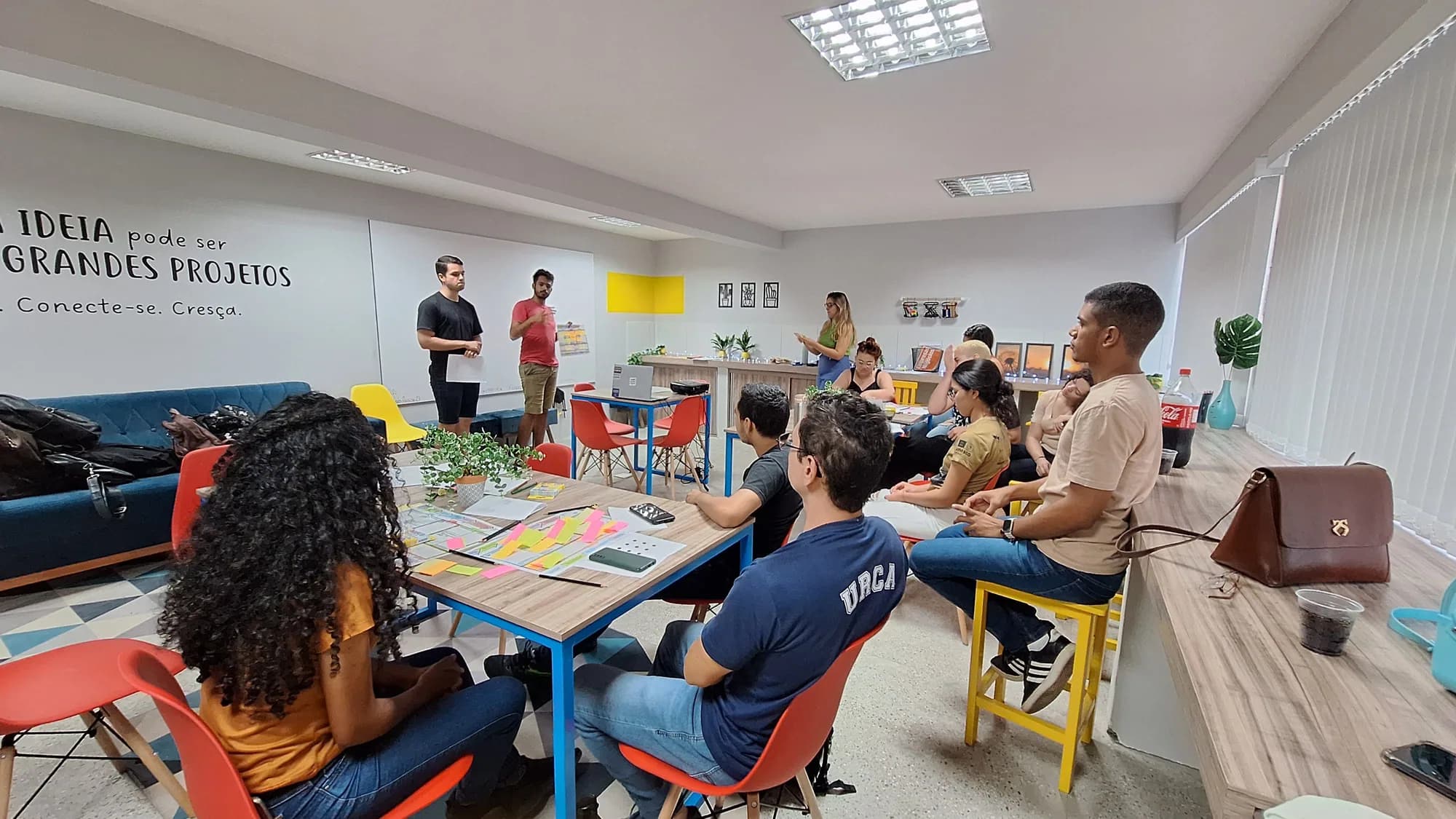 Pessoas conversam em torno de uma mesa com materiais de uma atividade colaborativa