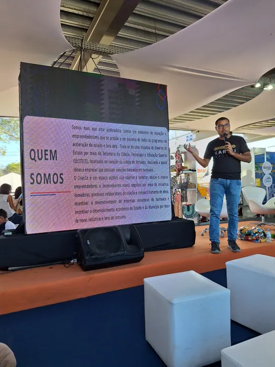 Participante apresenta a comunidade ao lado de um painel durante um encontro