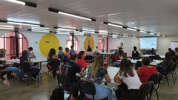 Participantes acompanham uma apresentação sentados em uma sala