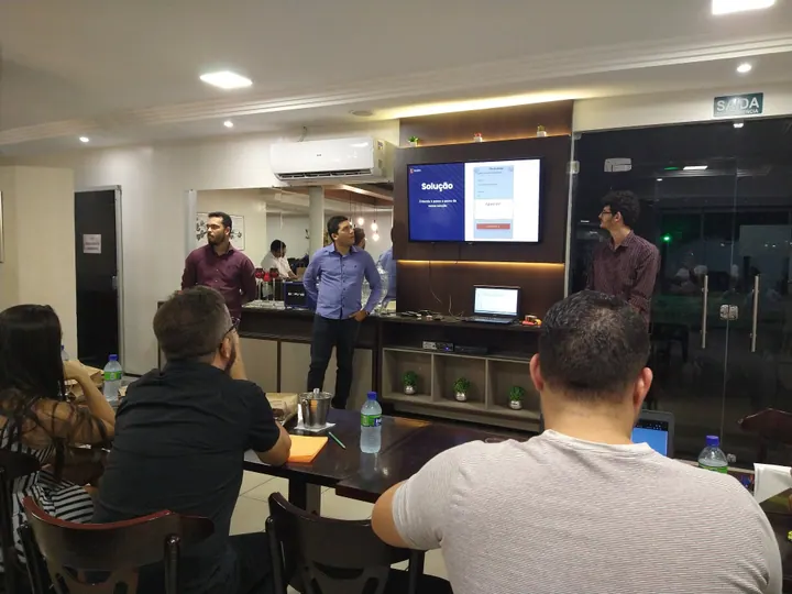 Pessoas acompanham uma apresentação com slides em uma sala de encontro