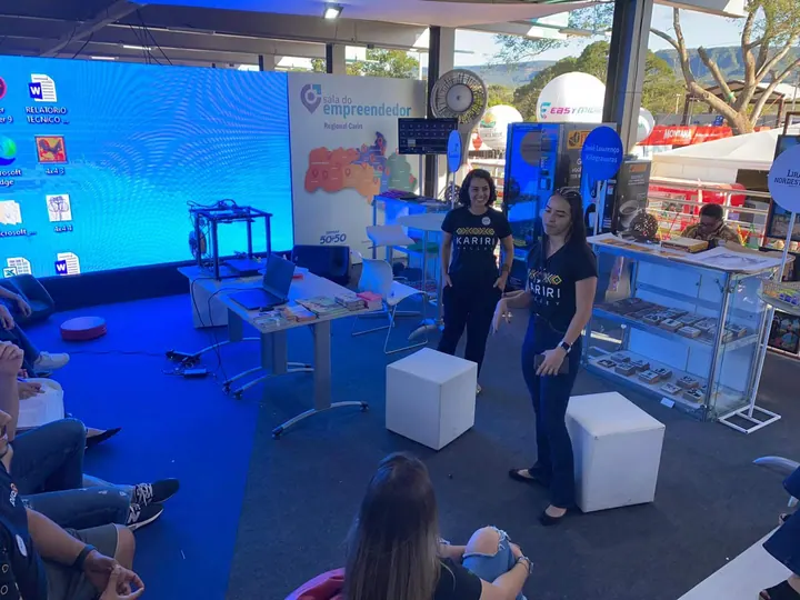Participantes da comunidade apresentam ideias junto a uma tela em um espaço de evento
