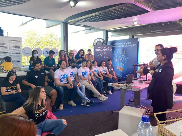 Participante com microfone conversa com pessoas sentadas em um espaço aberto de inovação