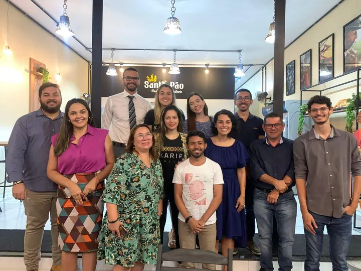 Grupo da comunidade reunido em uma sala com mesas, cadeiras e painéis