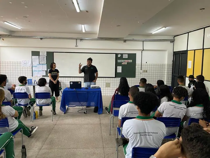 Participantes apresentam ideias diante de estudantes em uma sala de aula