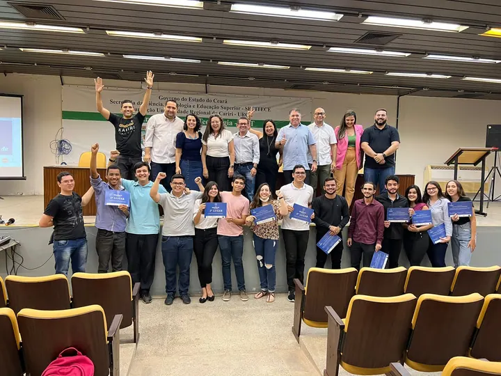 Grupo da comunidade reunido em um auditório, com participantes segurando certificados