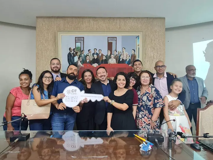 Participantes reunidos em uma sala de encontro, segurando uma chave simbólica