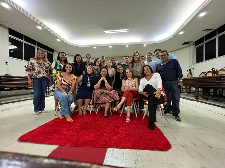 Grupo da comunidade reunido em cadeiras sobre um tapete vermelho