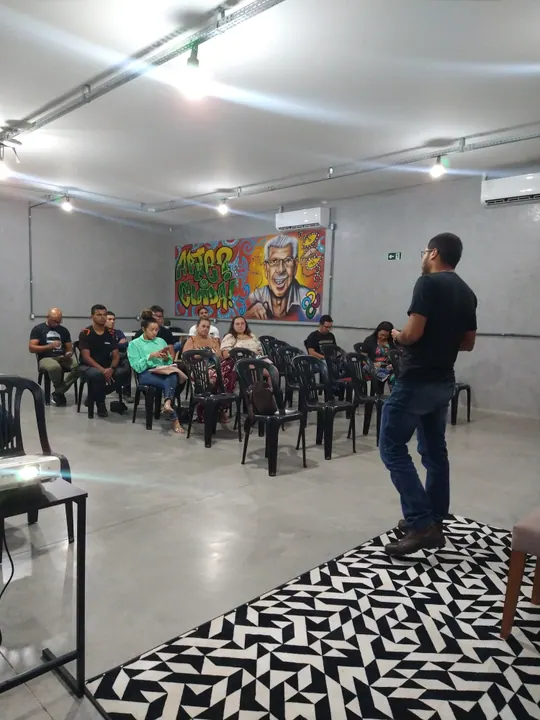 Participante fala a um público sentado em uma sala com painéis coloridos