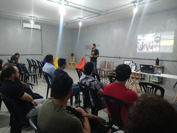 Participante apresenta ideias ao lado de uma projeção durante um encontro