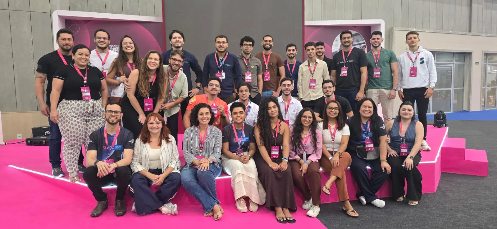 Pessoas da comunidade reunidas em um evento, sentadas e em pé sobre uma arquibancada rosa