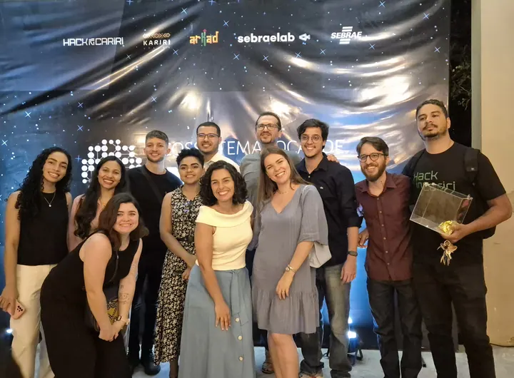 Participantes da comunidade reunidos em frente a um painel de evento
